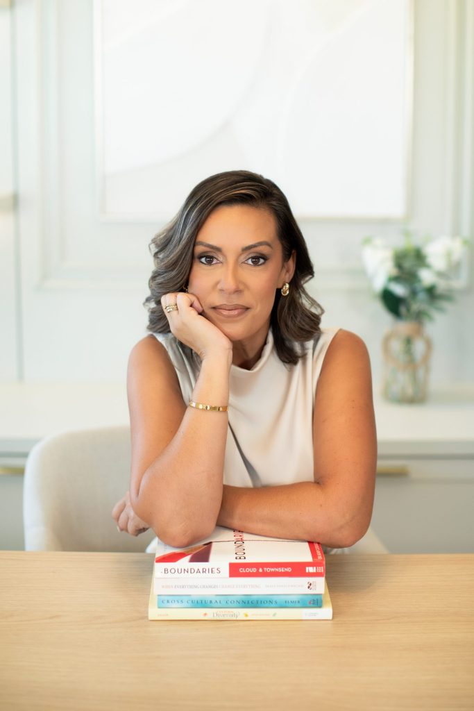 Débora Bueno, consultora da NeuroBridge, sentada à mesa com livros sobre conexões interculturais e diversidade cultural