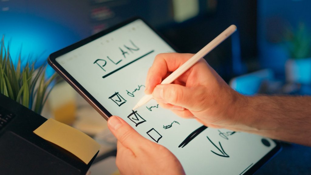Pessoa escrevendo uma lista de planejamento com caixas de seleção em um tablet